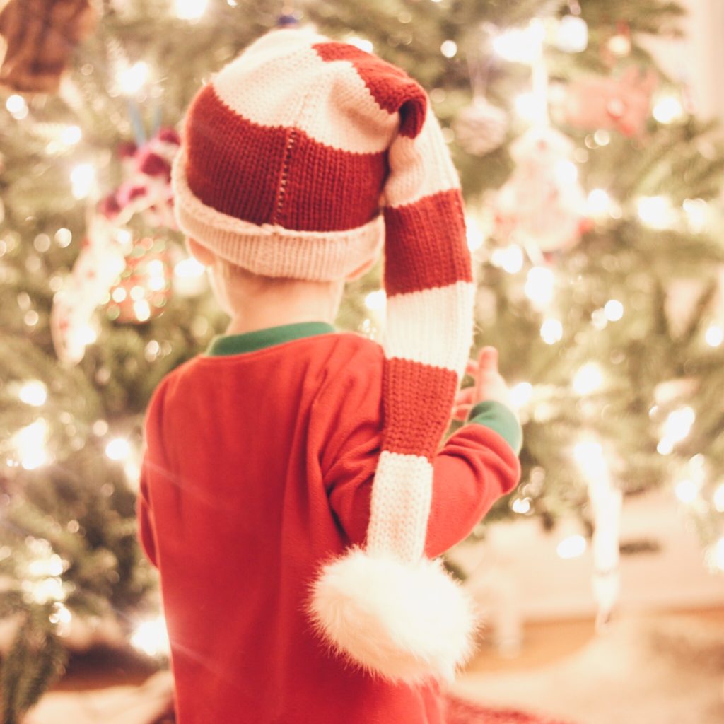 toddler in front of christmas tree in long striped knit santa hat