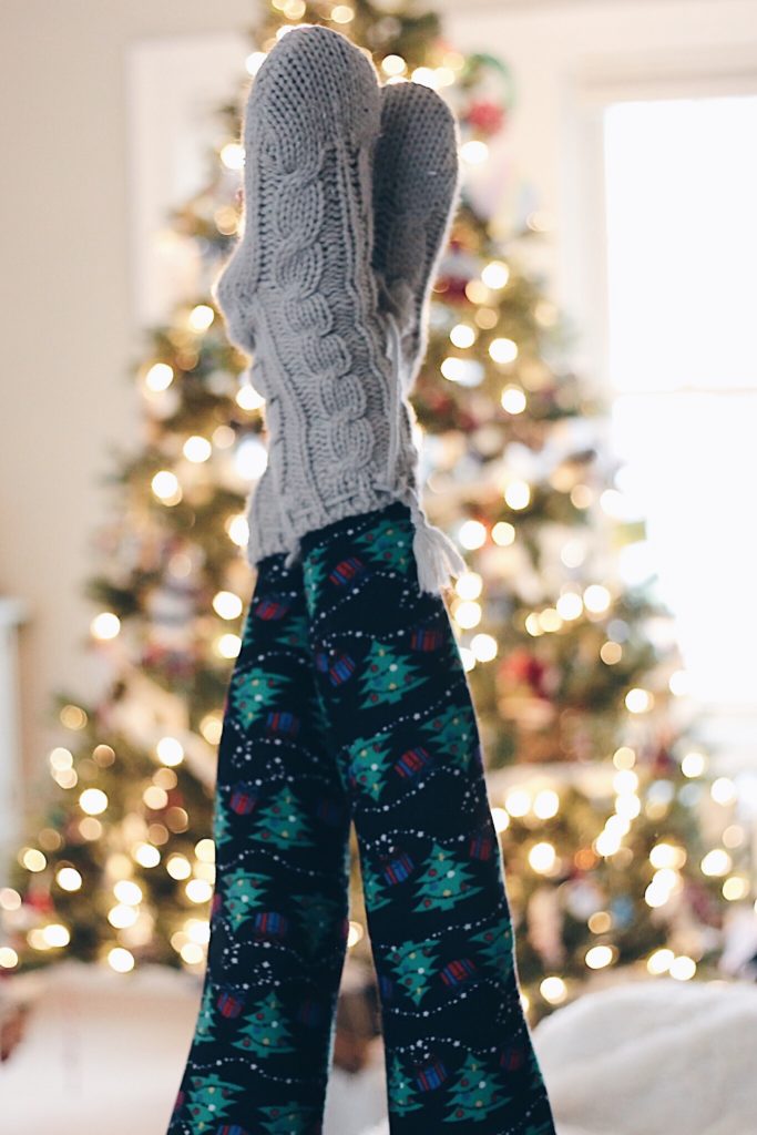 holiday theme party ideas - cozy ski lodge theme party ideas - christmas leggings and slipper socks in front of a Christmas tree - cozy holiday attire