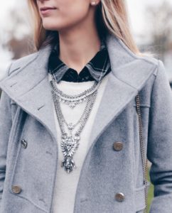 gray women's military coat with statement bib necklace over white crewneck sweater