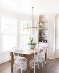 Dining area showcasing Benjamin Moore Edgecomb Gray cabinetry with gold hardware, a natural wood dining table, and white spindle chairs.