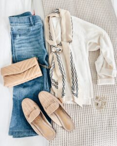 Neutral fall outfit flatlay featuring blue jeans, an ivory sweater, a chain-print scarf, quilted nude handbag, and beige mule loafers. A classic and chic outfit idea for women over 40.