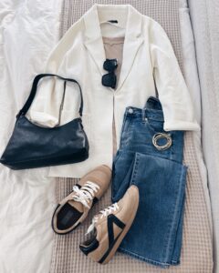 Casual chic outfit for women over 40 featuring a white blazer, fitted jeans, beige sneakers, and a black leather shoulder bag. A stylish way to wear a blazer with sneakers.