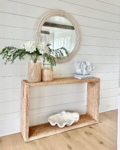 styled modern coastal console table with a round rope mirror, woven vases with white hydrangeas, a coral sculpture, and a giant clamshell accent