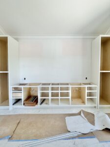 Built-in bathroom cabinetry with open shelves and plumbing installed, still awaiting drawer fronts and countertops in a newly built home.
