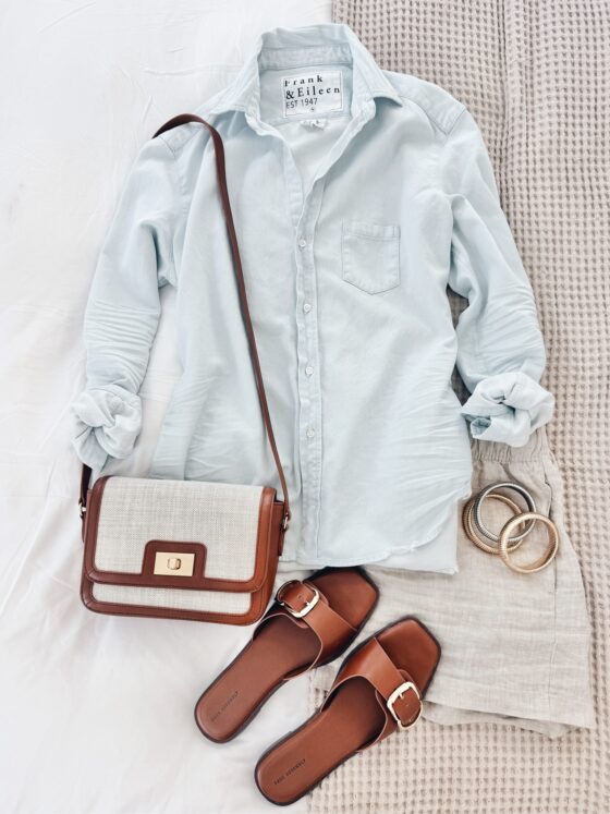 Relaxed summer outfit with a pale blue Frank & Eileen button-up shirt, beige linen shorts, tan slide sandals, a neutral crossbody bag with gold hardware, and gold bangles.