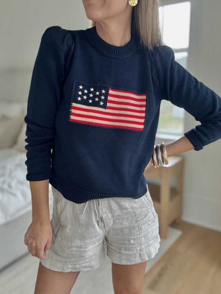Navy puff sleeve flag sweater from Tuckernuck with linen drawstring shorts and gold accessories